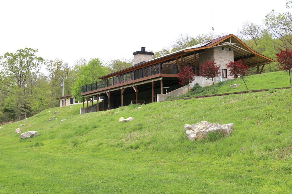 a large stone and wood outdoor pavillion built on a grassy hillside