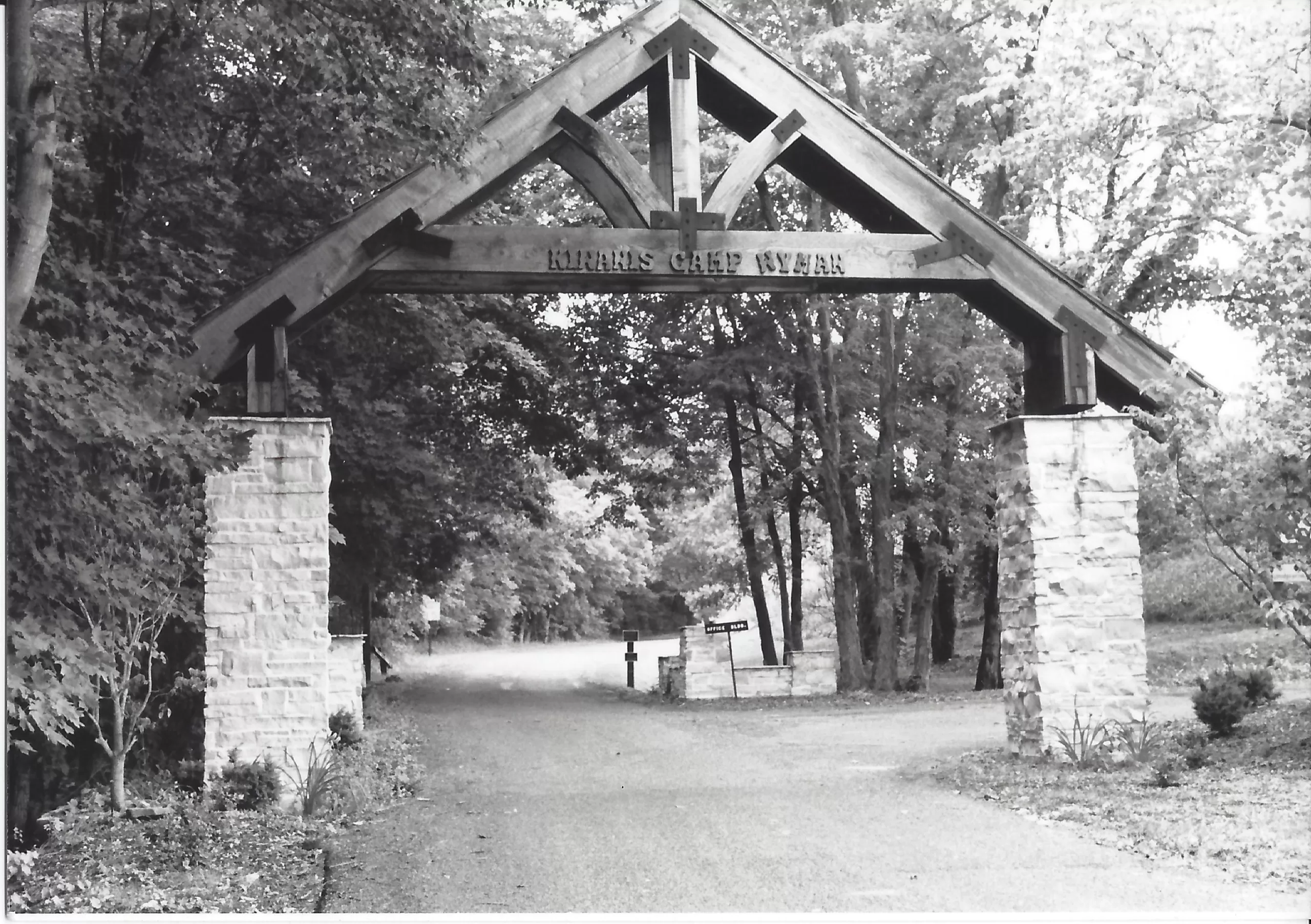 Image of a rustic, stone and wooden archway over a roadway. The text on the archway reads "Kiwanis Camp Wyman"