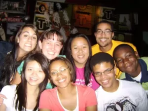 A group of high school aged men and women group together and smile at the camera.