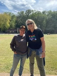 Kelly Williams and Laura Arnold at camp with trees behind.