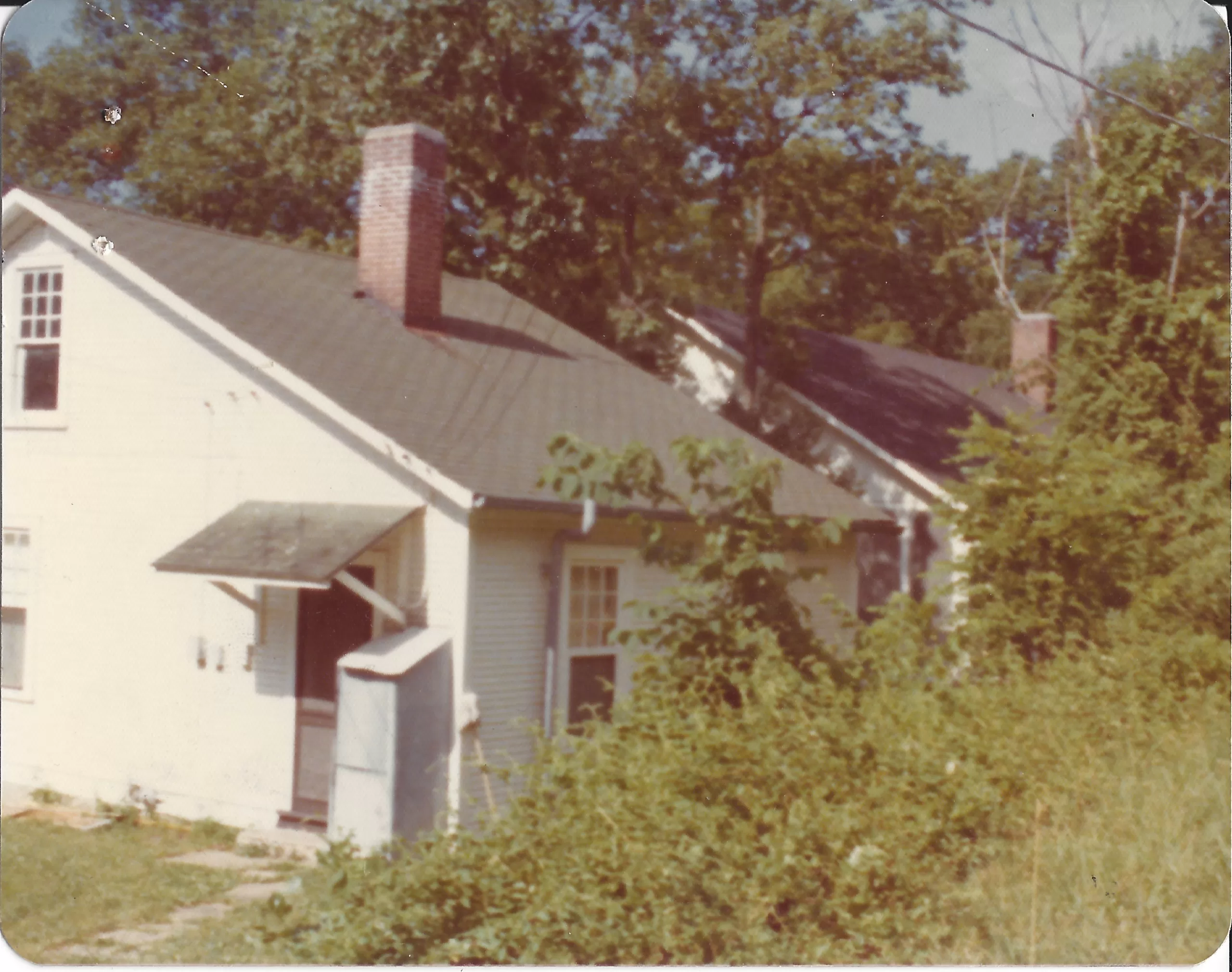 An old photograph of a small white buildling behind bushes