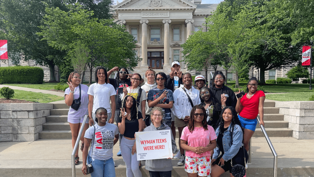 group of teens posing in front of an academic building