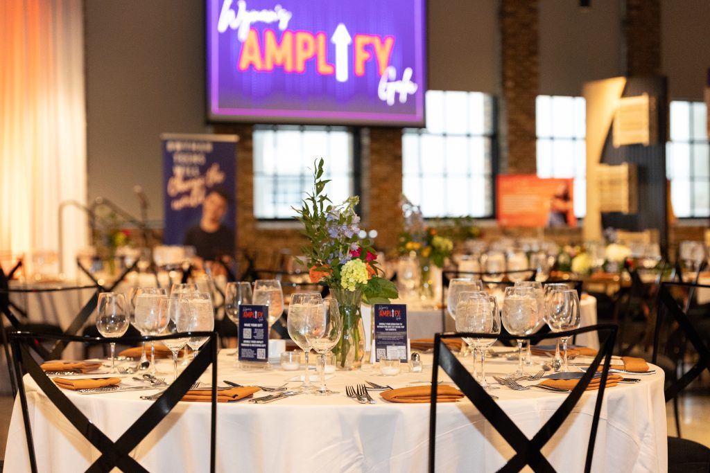 an image of an event set up before guests arrive, showing table settings and blurred banners and video screens in the background