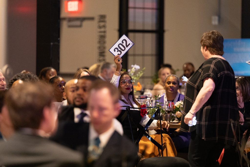a woman holds up a bidding card during a gala donation pledge event